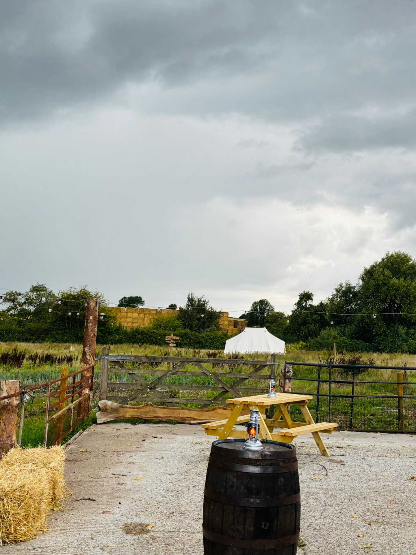 Laxstone Ranch entrance with a wooden gate, hay bales, barrel lantern and a bell tent set against open Nottinghamshire farmland